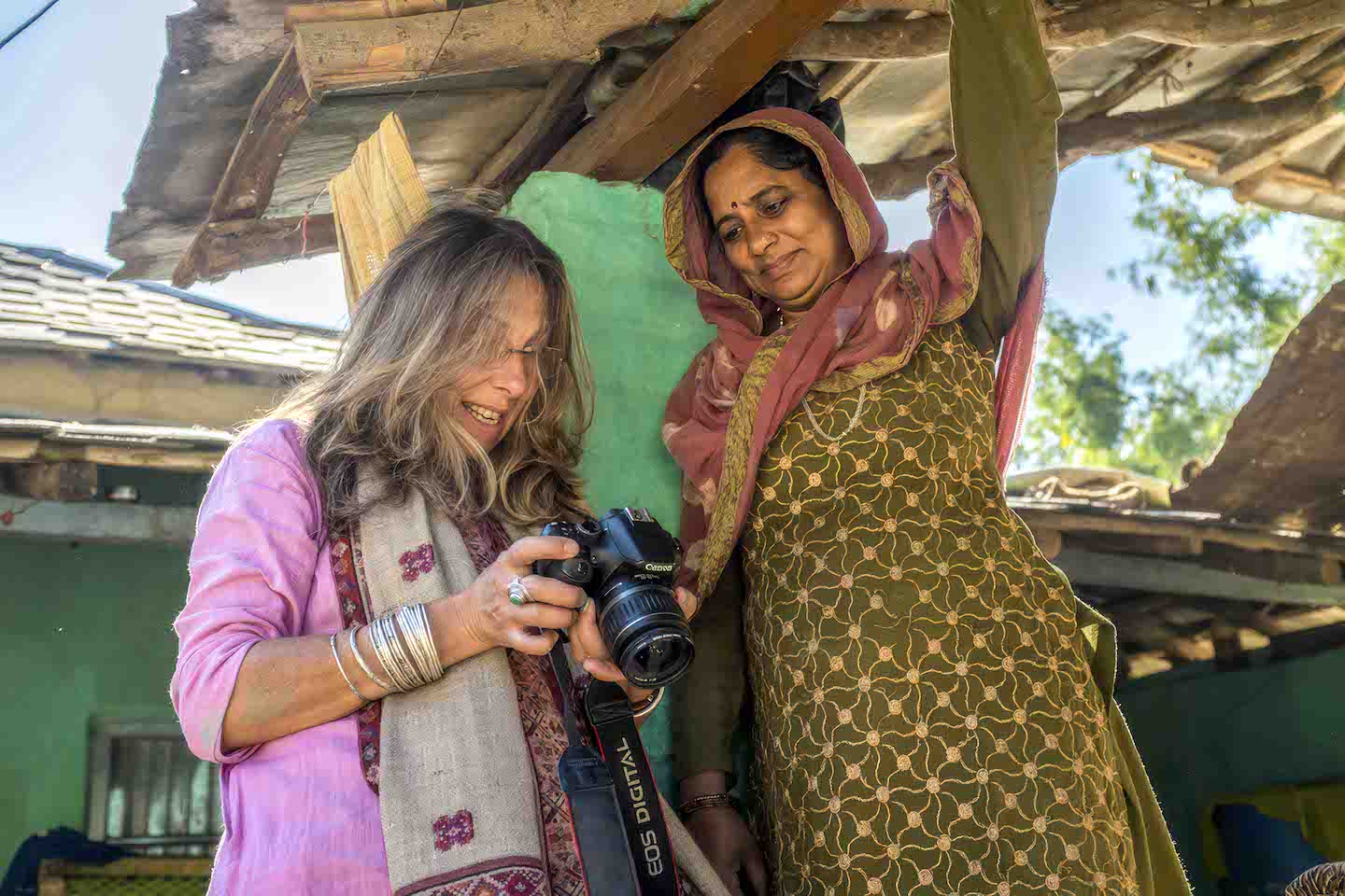 Foreign photographer sharing camera image with local Indian woman in traditional dress, cultural exchange in rural village