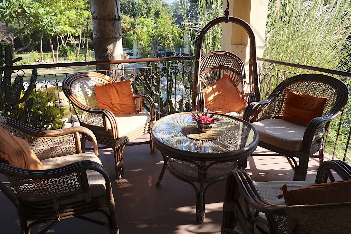 Outdoor veranda with wicker chairs, swing seat, and garden view at Basunti Resort Himachal Pradesh