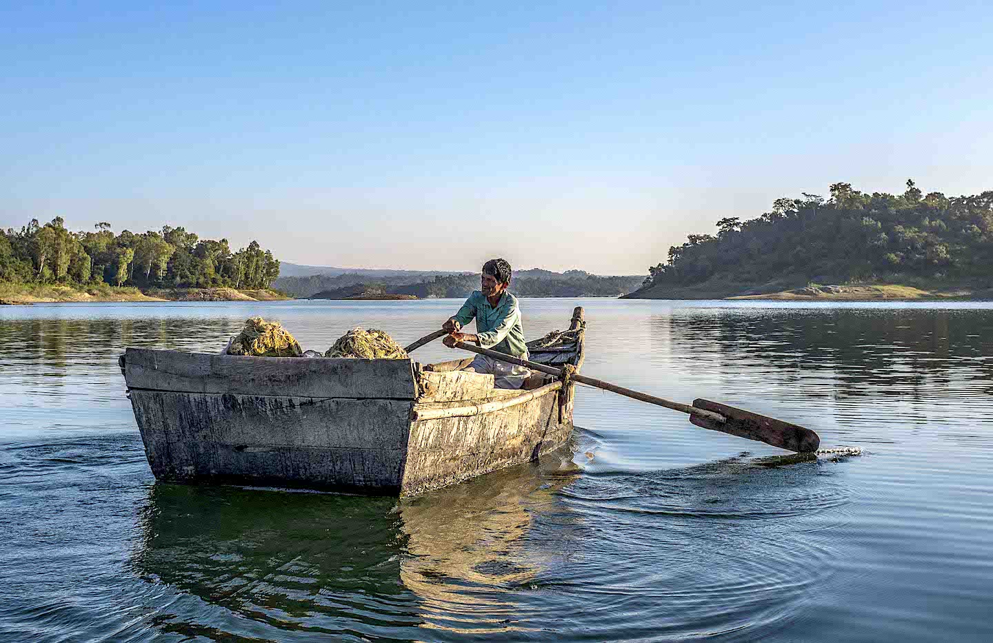 Indian fisherman rows wooden boat on calm lake at sunrise