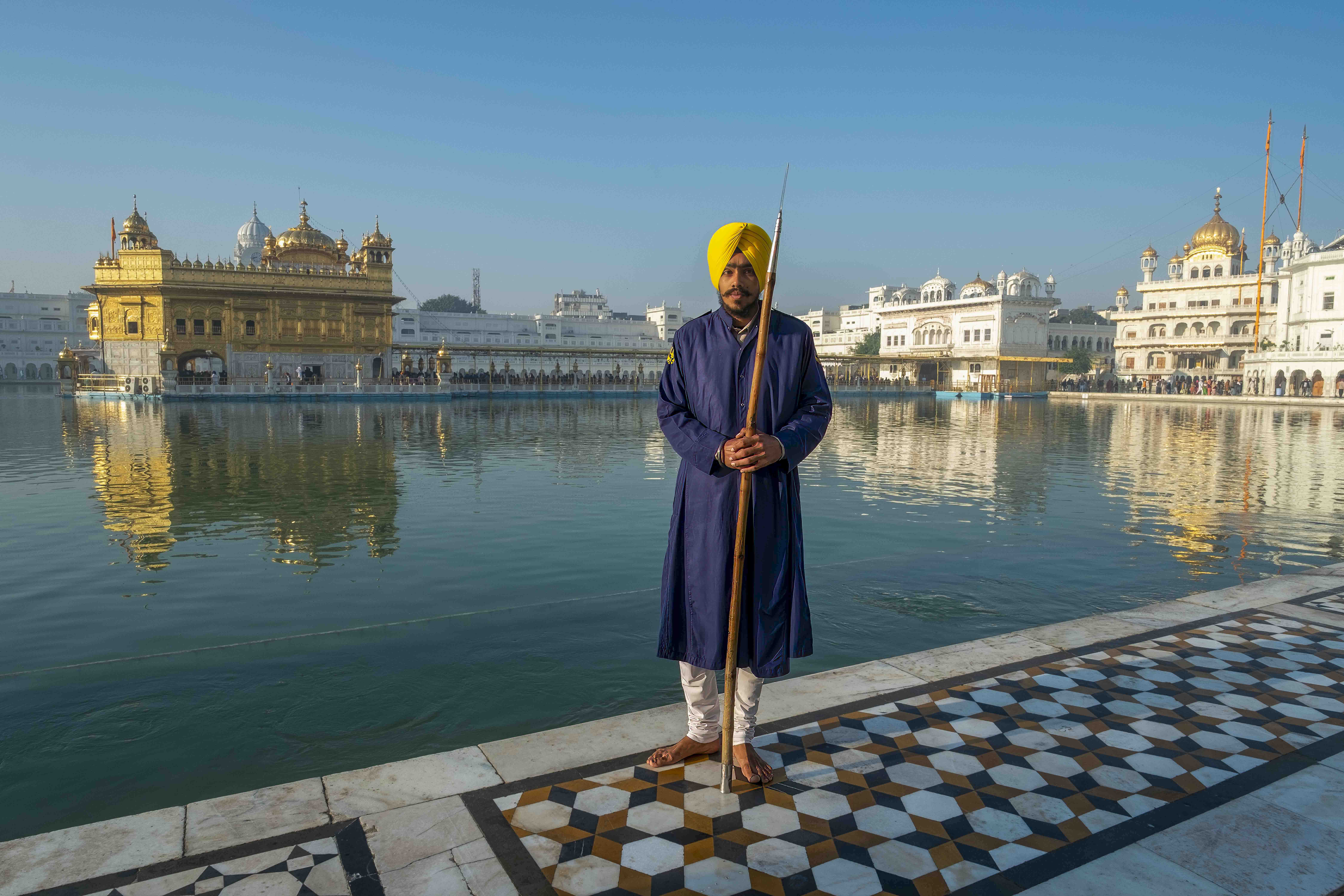 Sikh guard with yellow turban holding spear in front of Golden Temple Amritsar, Punjab India