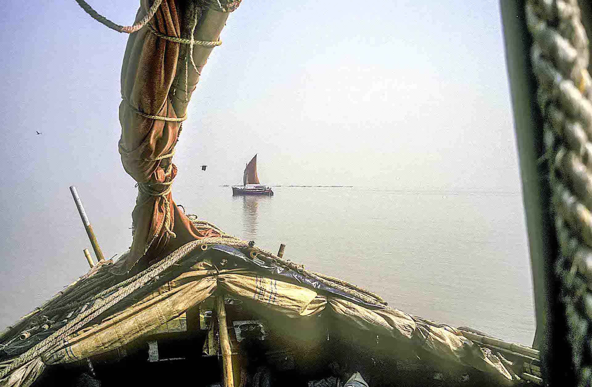 Traditional wooden sailboat on calm river viewed from another boat, rustic fishing vessel in India